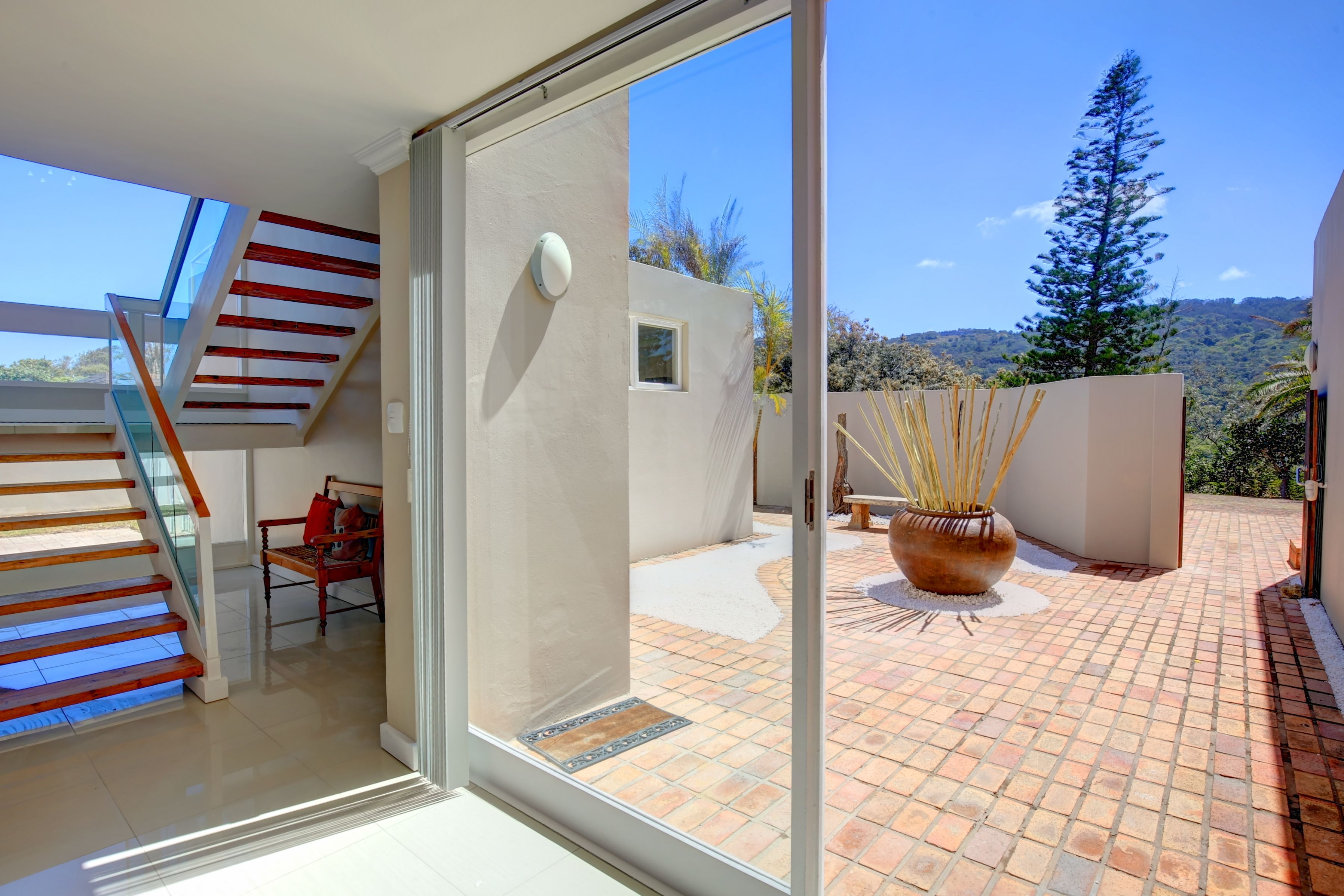 A modern interior with a glass door leading to a patio area, a wooden staircase, and a view of the outdoors.