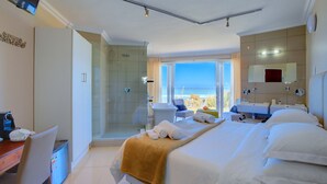 A hotel room with a bed, a desk, a chair, a shower area, and a view of the ocean. - Dune Villa Wilderness (Wilderness)