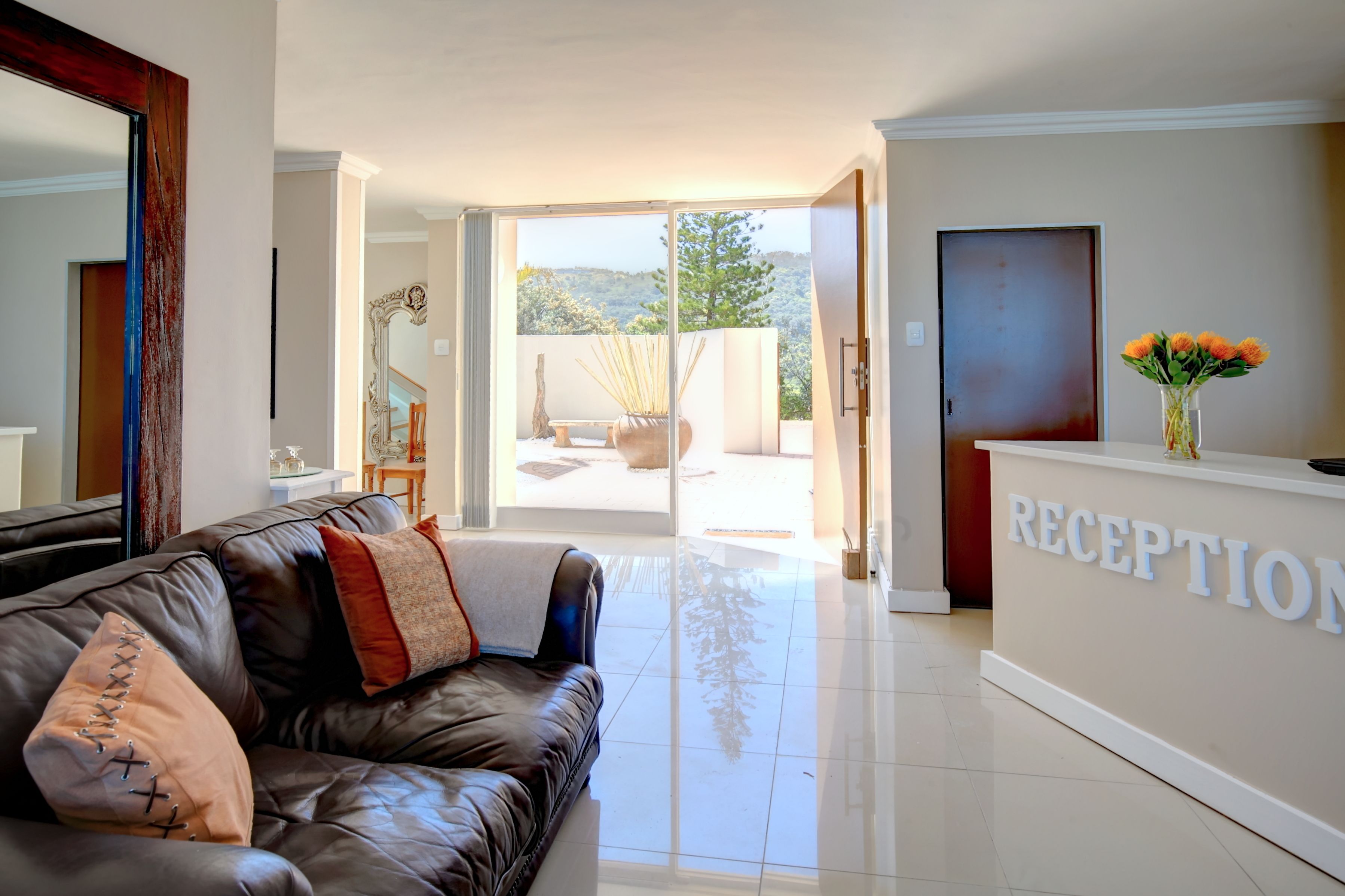A reception area with a leather sofa, a reception desk, and a view of a patio with outdoor furniture.
