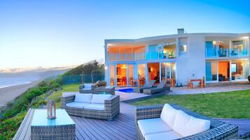 A modern two-story house with a balcony overlooking the beach, outdoor furniture, and a pool.