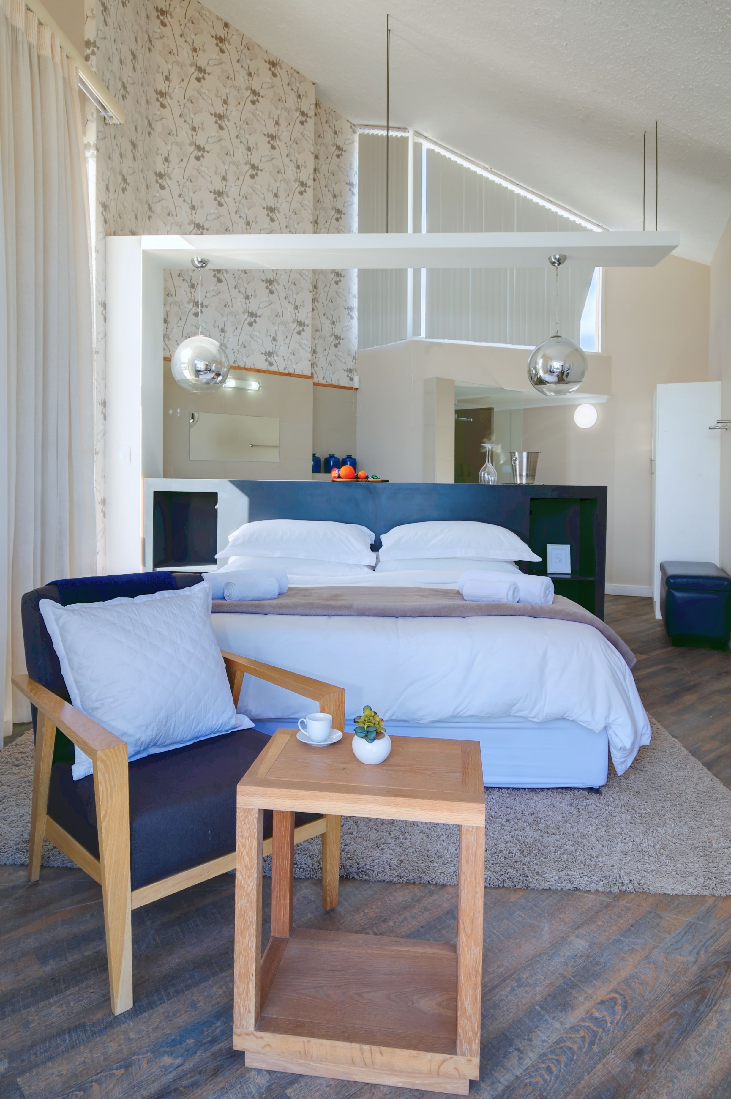 Et moderne hotelværelse med en seng, et træsidebord, en stol, et lille bord og et spejl.