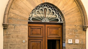Une grande porte en bois, surmontée d’un vitrail décoratif, est encastrée dans un mur de pierre.