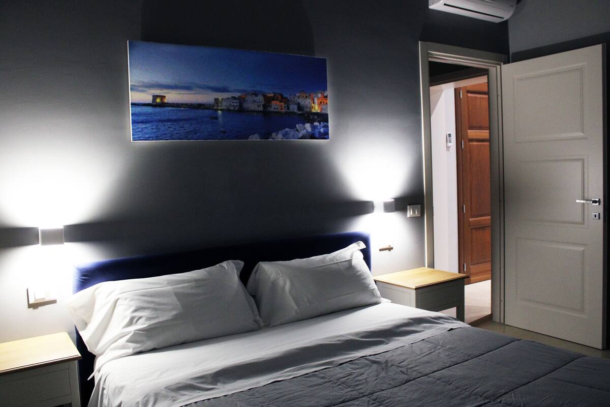Ein Schlafzimmer mit Bett, Nachttischen, einem Wandbild und einer Tür.