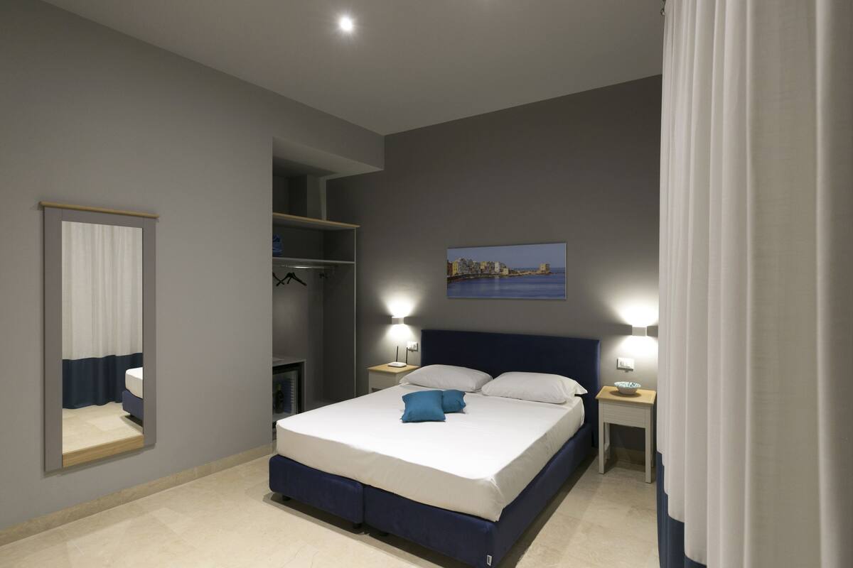 Ein modernes Schlafzimmer mit einem großen Bett, Nachttischlampen, einem Spiegel und einem Stadtbild an der Wand.