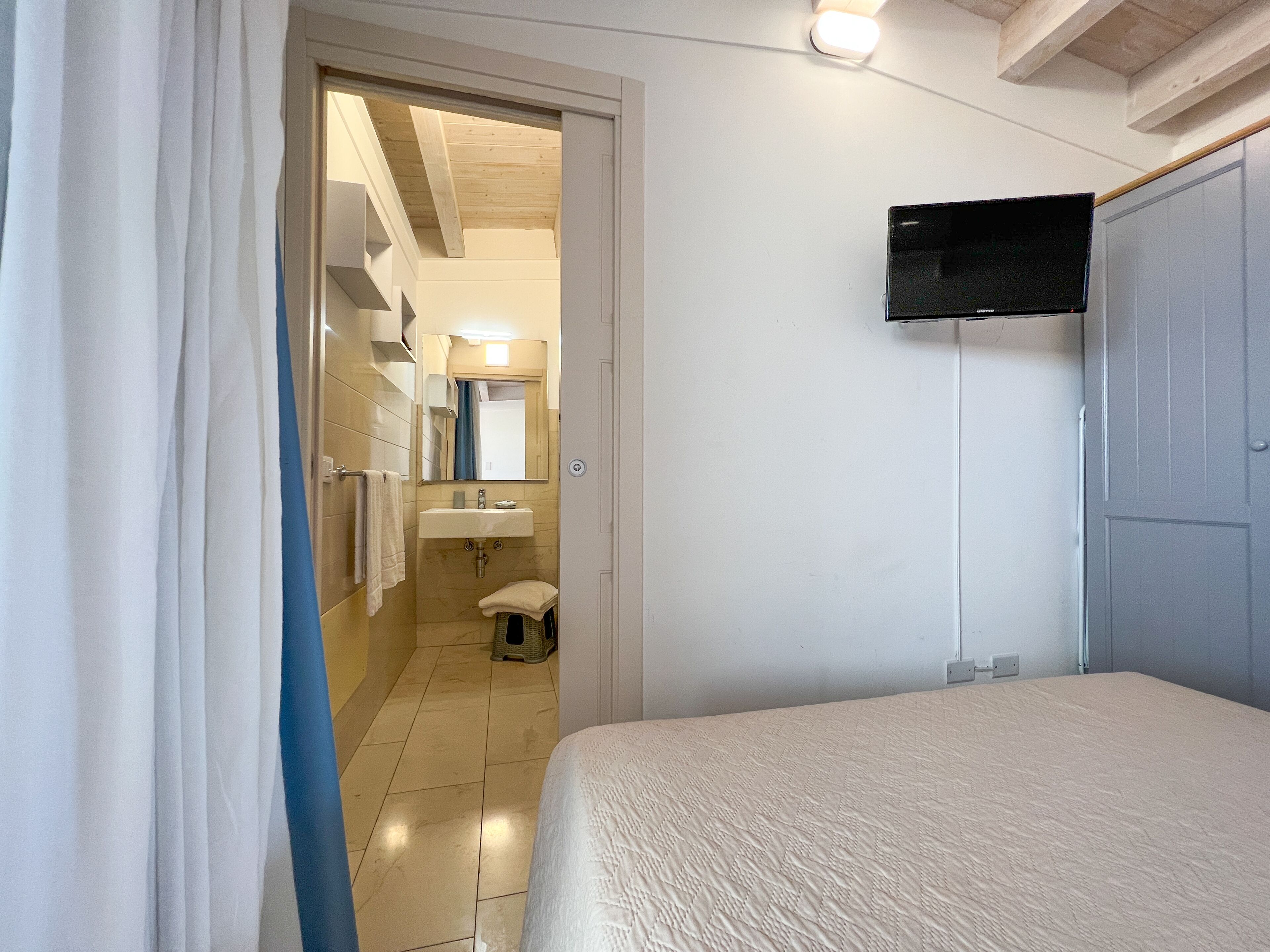 A bedroom with a bed, a television mounted on the wall, and a bathroom visible through an open door.