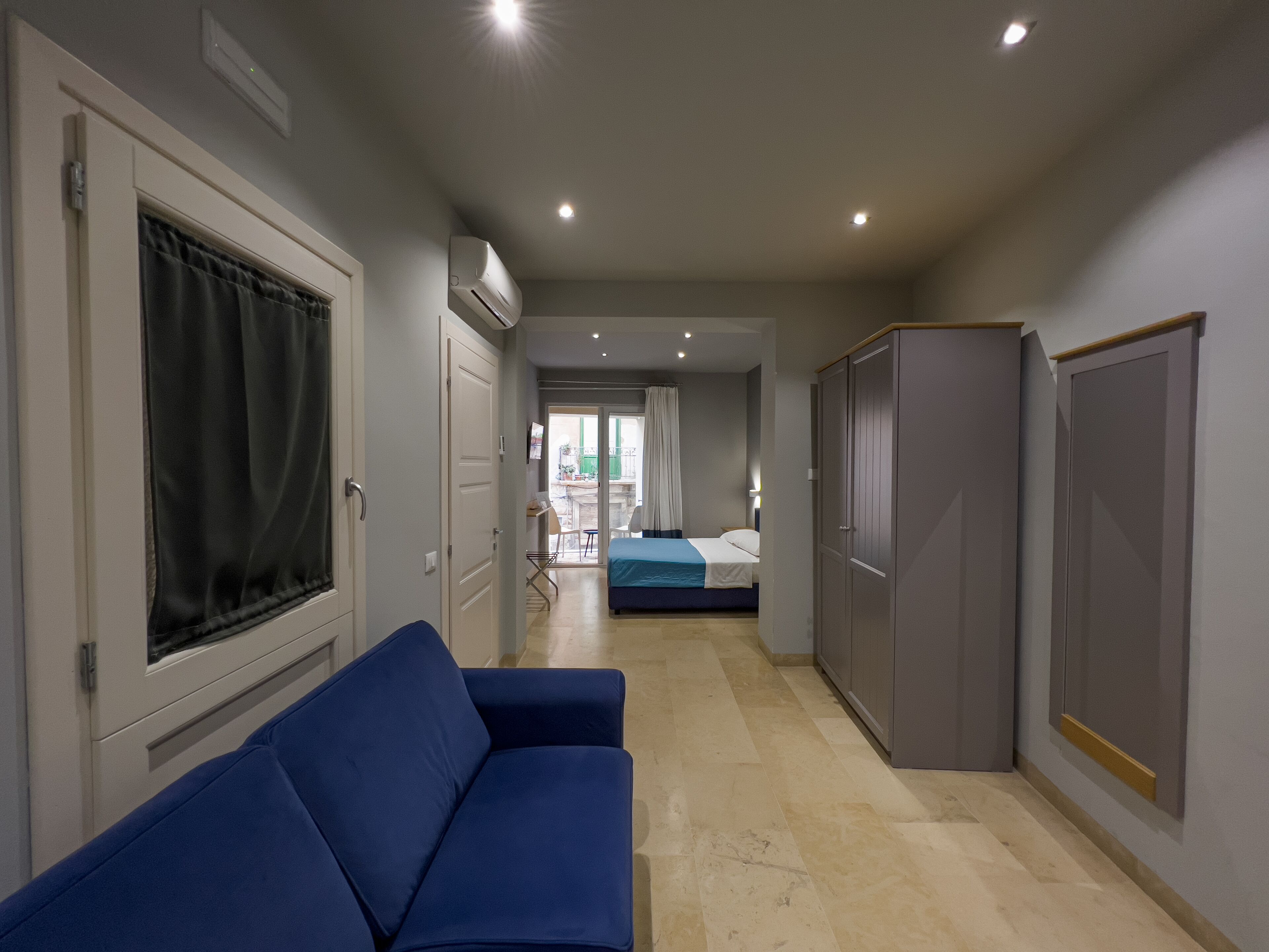 A hallway with a blue sofa, a wardrobe, and a bed in the background.