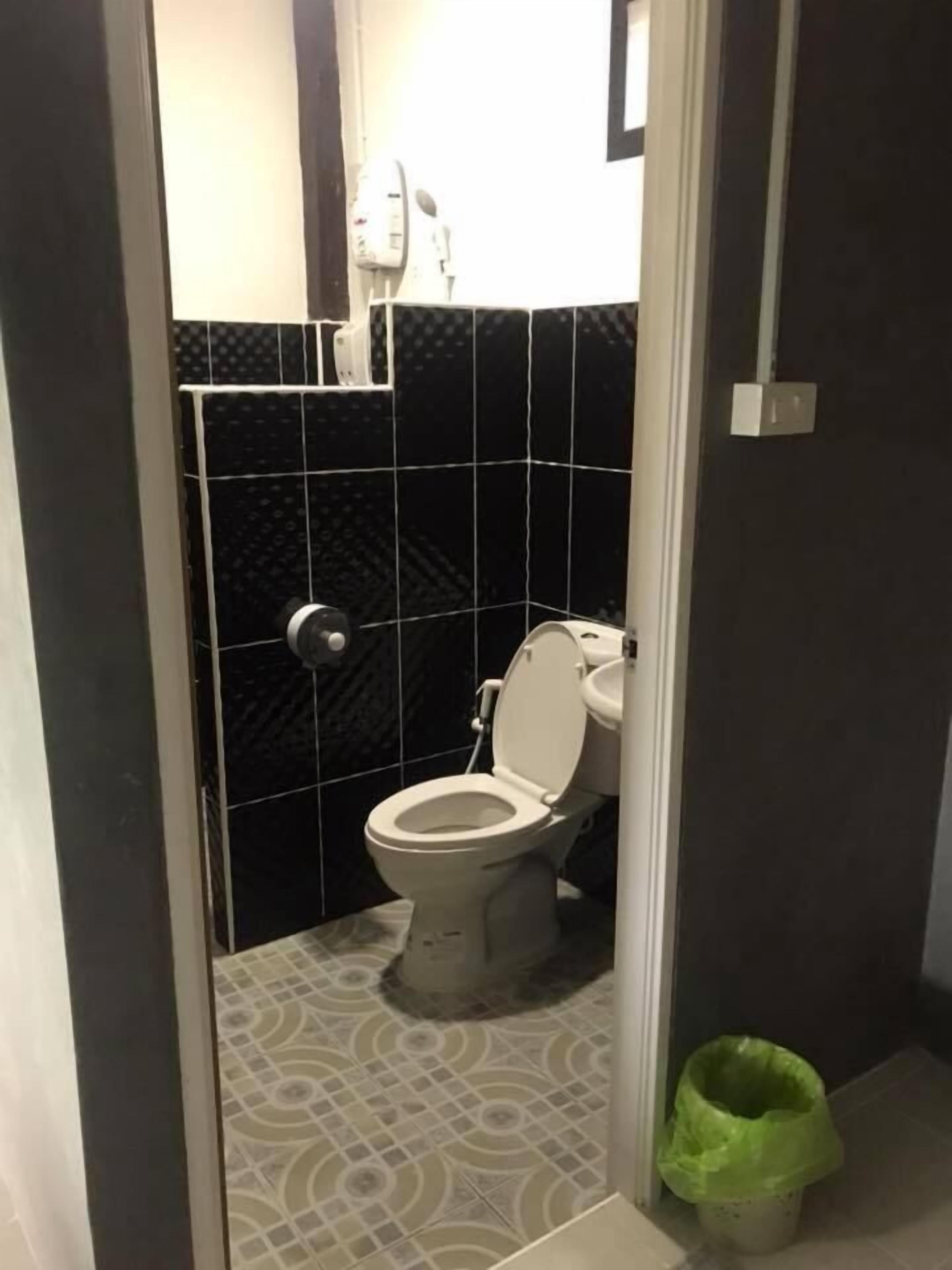 Un baño con inodoro, un cubo de basura y piso estampado.