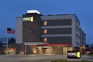 A modern hotel building with a sign reading "HOME 2 Suites by Hilton".
