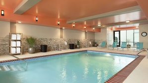 An indoor swimming pool with a tiled edge, lounge chairs, and a stone wall backdrop. - Home2 Suites by Hilton Leavenworth Downtown (Leavenworth)