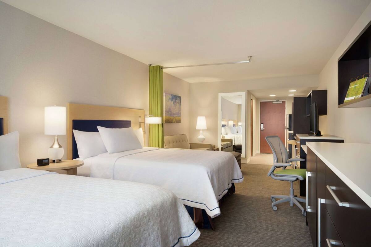 A hotel room with two beds, a desk, a chair, a TV, and a mirror.