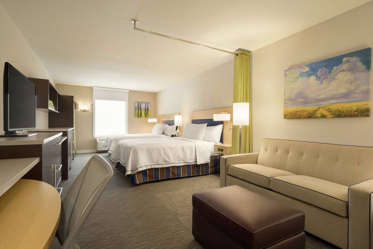 A hotel room with a bed, a sofa, a desk, a television, and a painting on the wall.