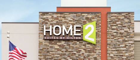 Un edificio con un cartel que dice "HOME 2 Suites by Hilton" y una bandera estadounidense.
