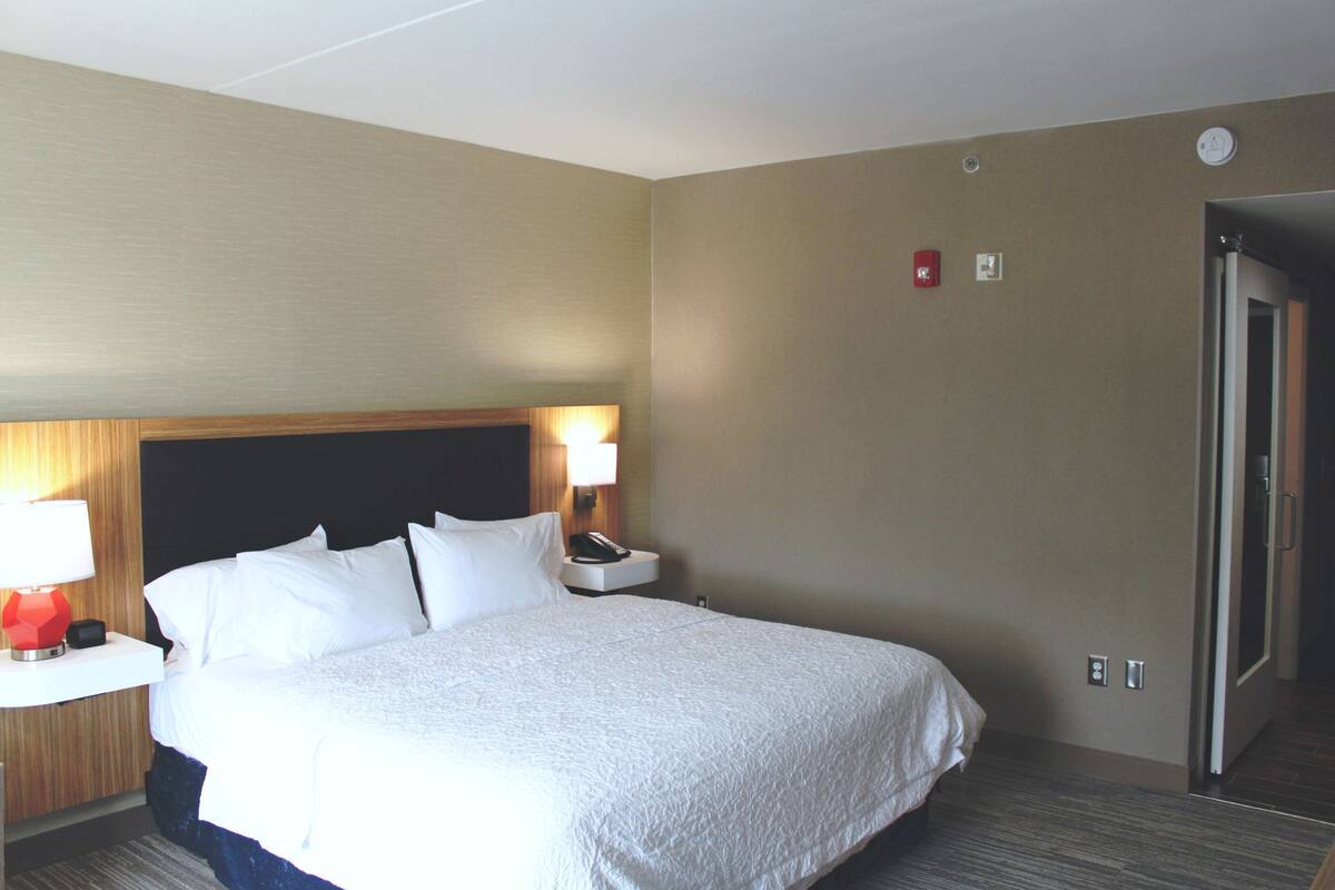 A hotel room with a large bed, a nightstand with a lamp, and a door.