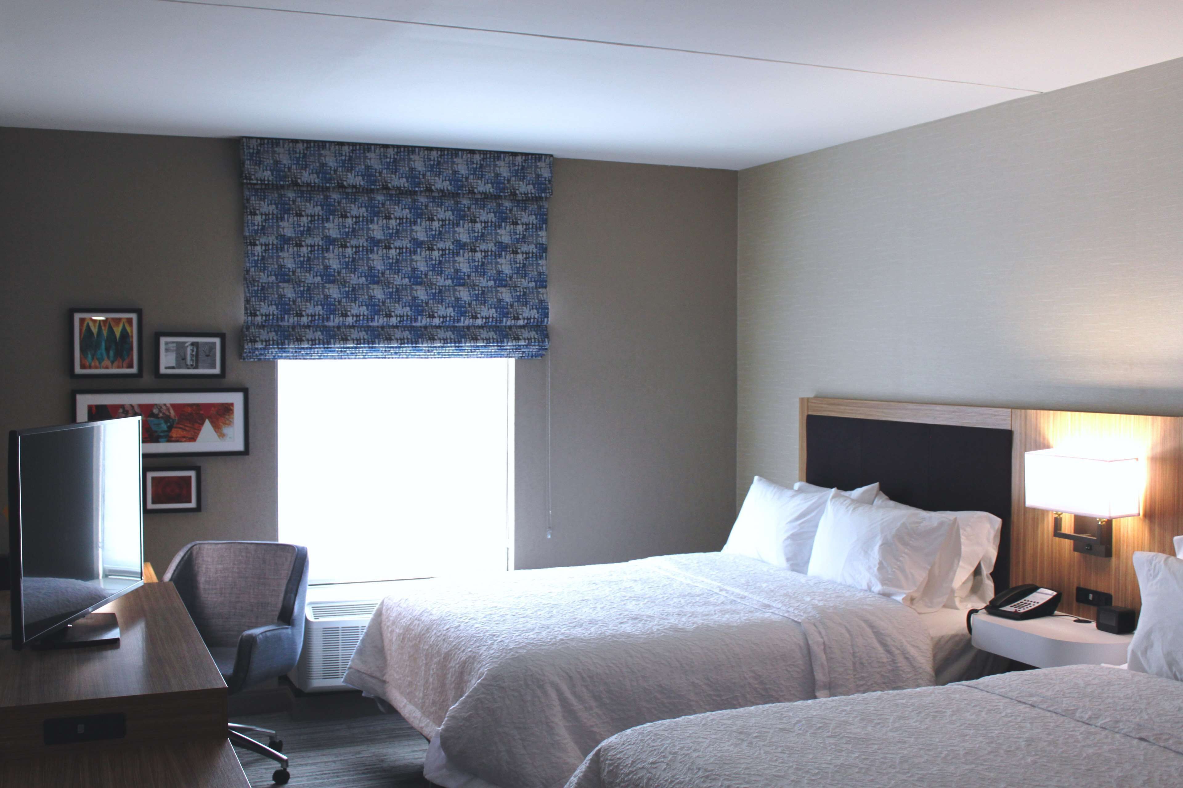 A hotel room with two beds, a desk with a computer, a TV, and a lamp.