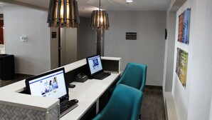 A reception desk with two computer monitors, a telephone, and a keyboard. There are two teal chairs and a hanging light fixture above.