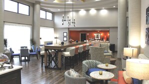 A spacious hotel lobby with a bar area, seating arrangements, and a modern ceiling design.