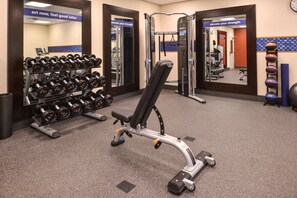 Ein Fitnessraum mit Krafttrainingsgeräten, einer Bank und Kurzhanteln.