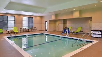 An indoor swimming pool with clear lane markings, a changing room with a shower, and several seating areas with chairs.