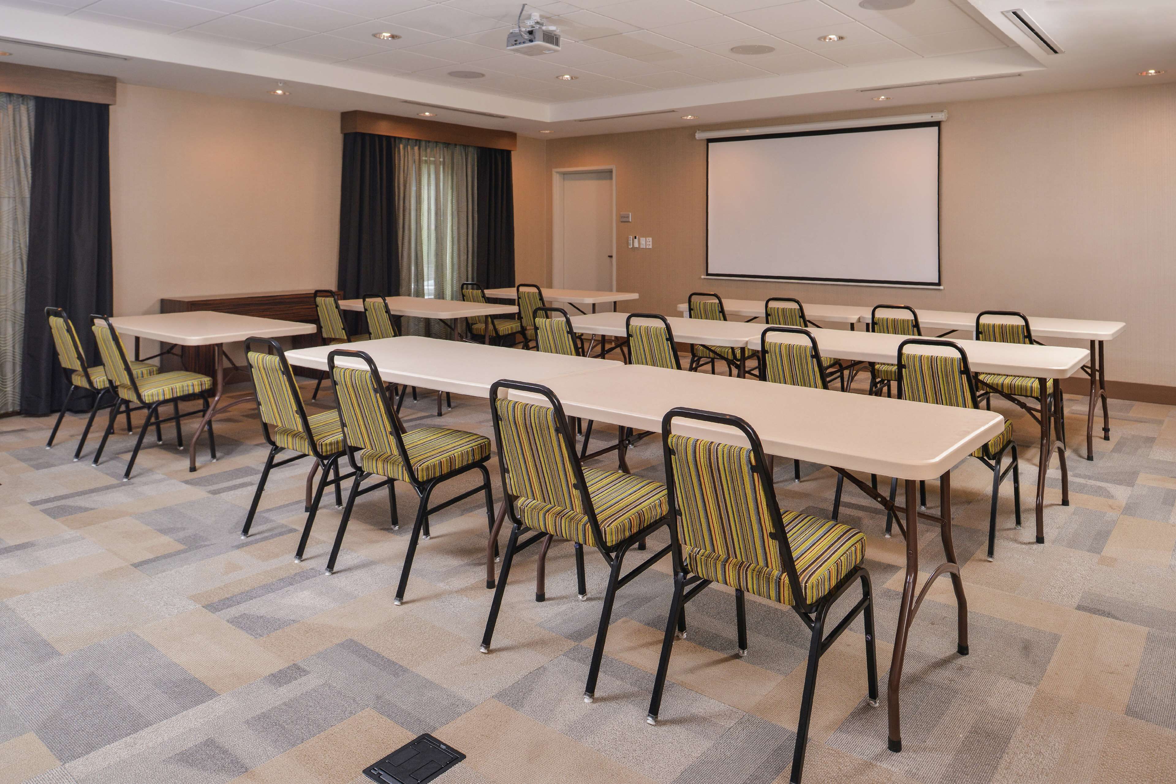 Ein Konferenzraum mit langen Tischen, Stühlen, einer Projektionsleinwand und einem Teppichboden.