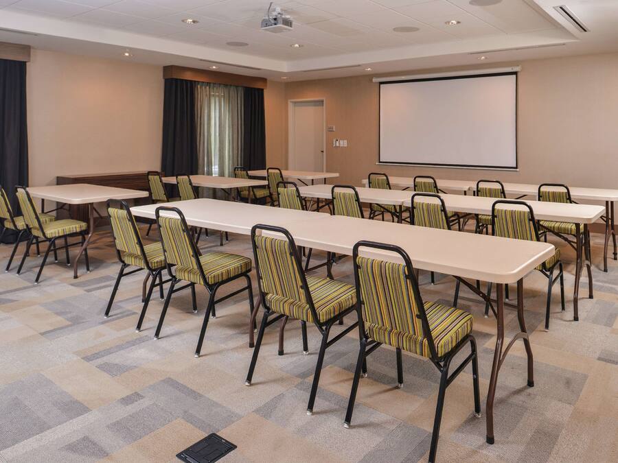 Ein Konferenzraum mit langen Tischen, Stühlen, einer Projektionsleinwand und einem Teppichboden.