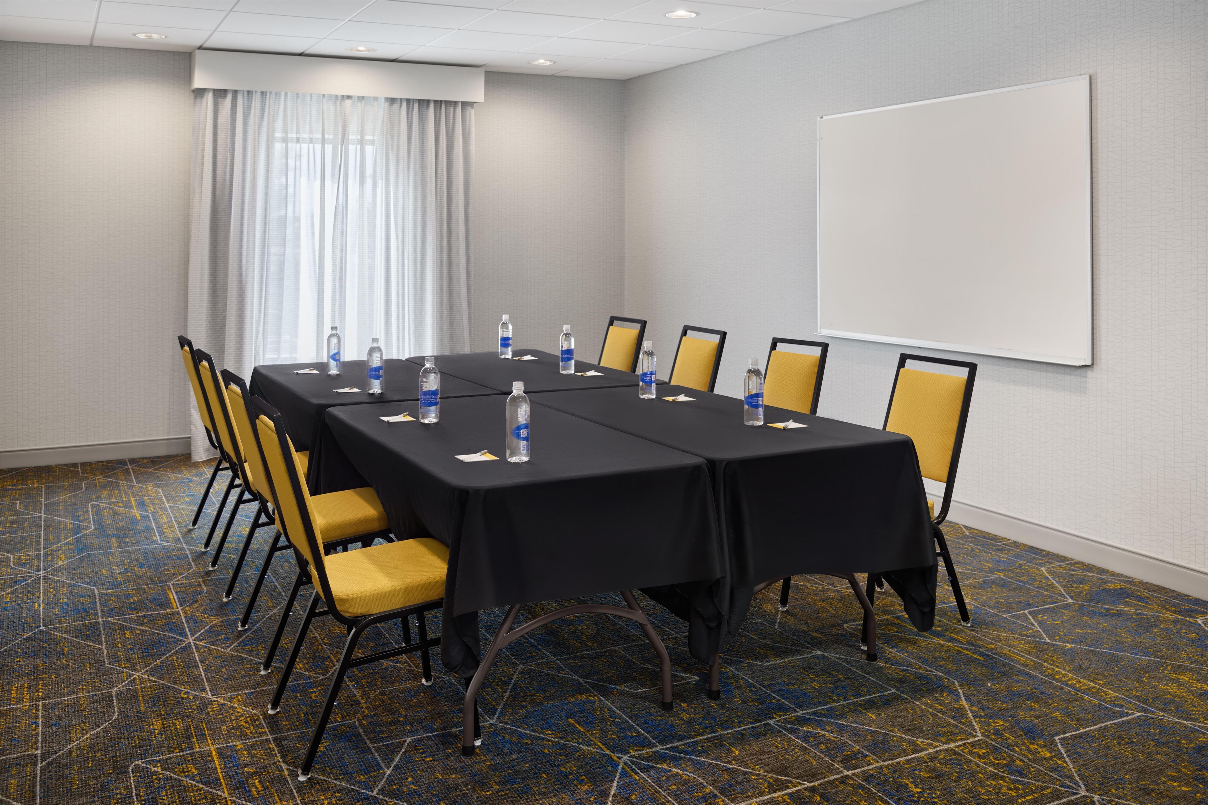 A conference room with a long table, chairs, water bottles, and a whiteboard.