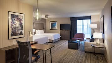 A hotel room with a bed, desk, chair, sofa, TV, and artwork on the walls.