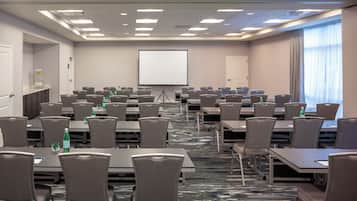 A conference room with multiple tables and chairs, a projector screen, and a water dispenser.