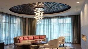 A modern living room with a sectional sofa, armchairs, a coffee table, and a unique ceiling design. - Homewood Suites by Hilton Needham Boston (Needham)