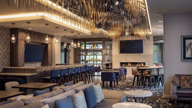 A modern bar area with seating, a fireplace, and a large TV screen. - Homewood Suites by Hilton Needham Boston (Needham)