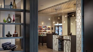 A hotel lobby with a reception desk, shelves with decorative vases, and a variety of amenities including snacks and beverages. - Homewood Suites by Hilton Needham Boston (Needham)