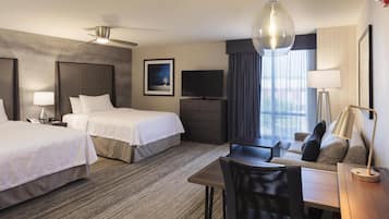 A hotel room with two beds, a desk, a chair, a television, a ceiling fan, and a window with curtains.