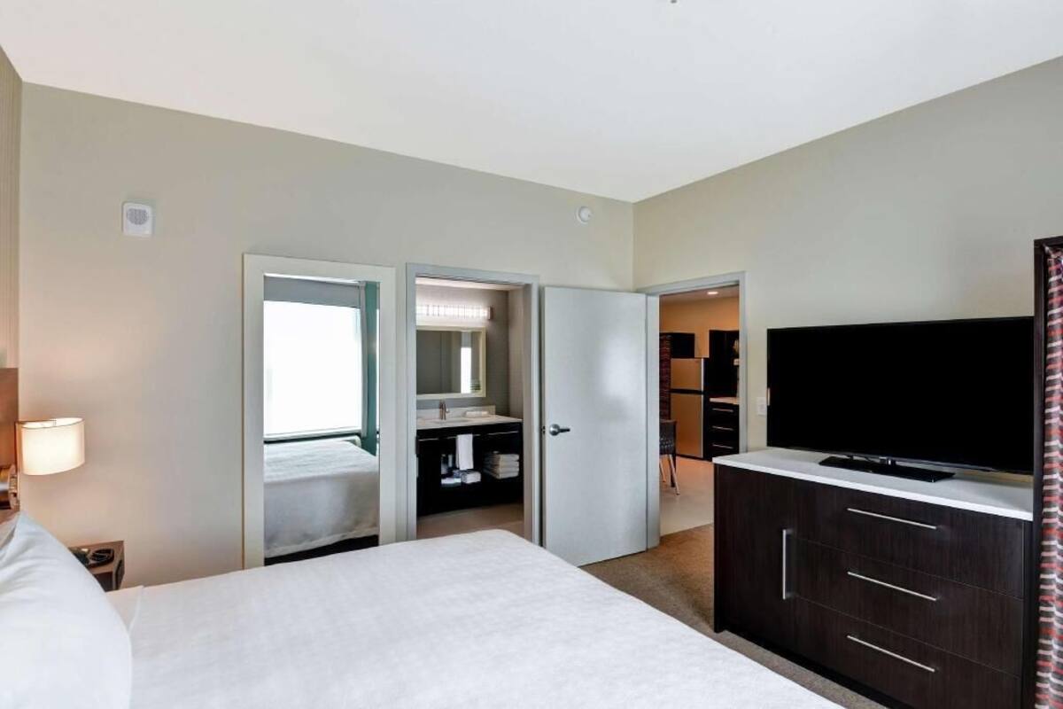 Habitación de hotel con cama, televisor, armario y baño visible a través de una puerta abierta.