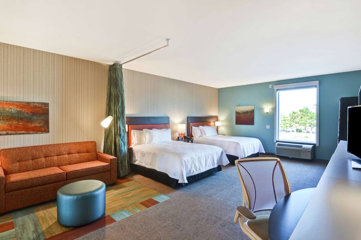 Habitación de hotel con dos camas, un sofá, un televisor y un ventanal grande.
