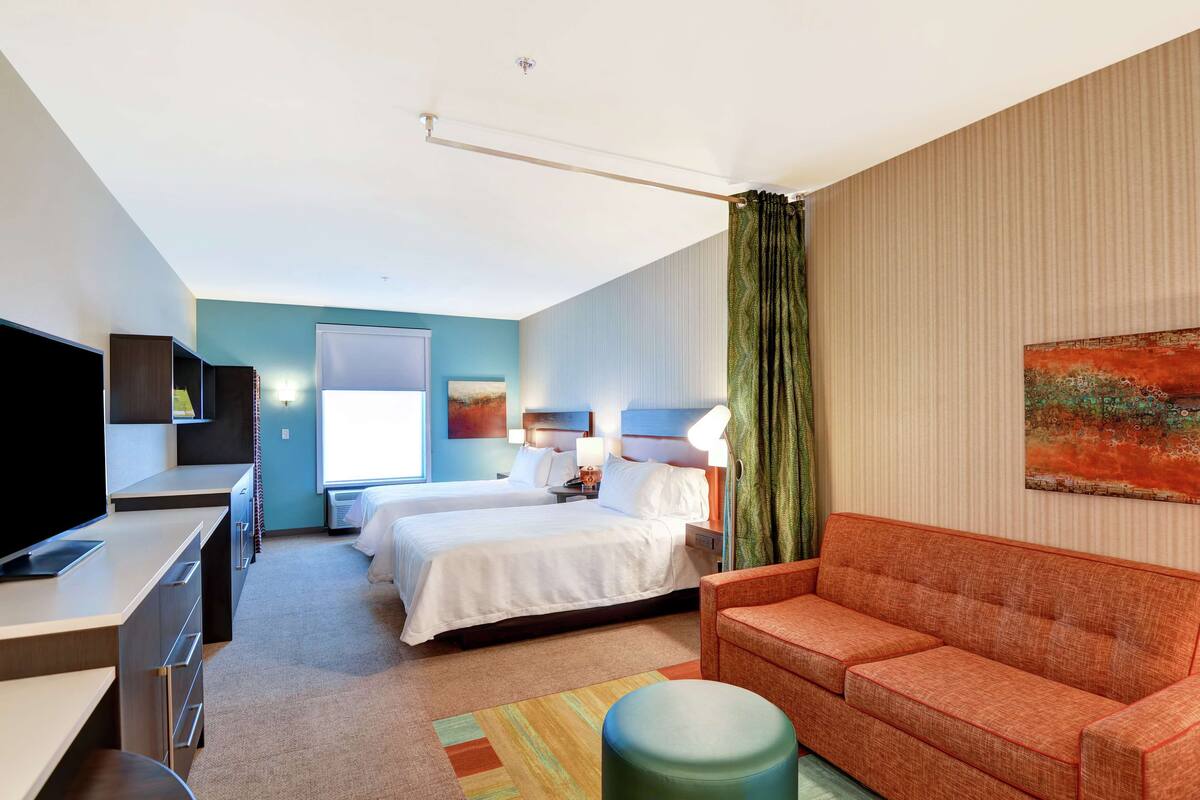 Habitación de hotel con dos camas, un escritorio, un sofá y un televisor.
