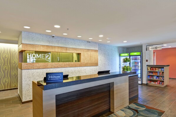 Zona de recepción de un hotel con mostrador, minibar y quiosco de autoservicio.