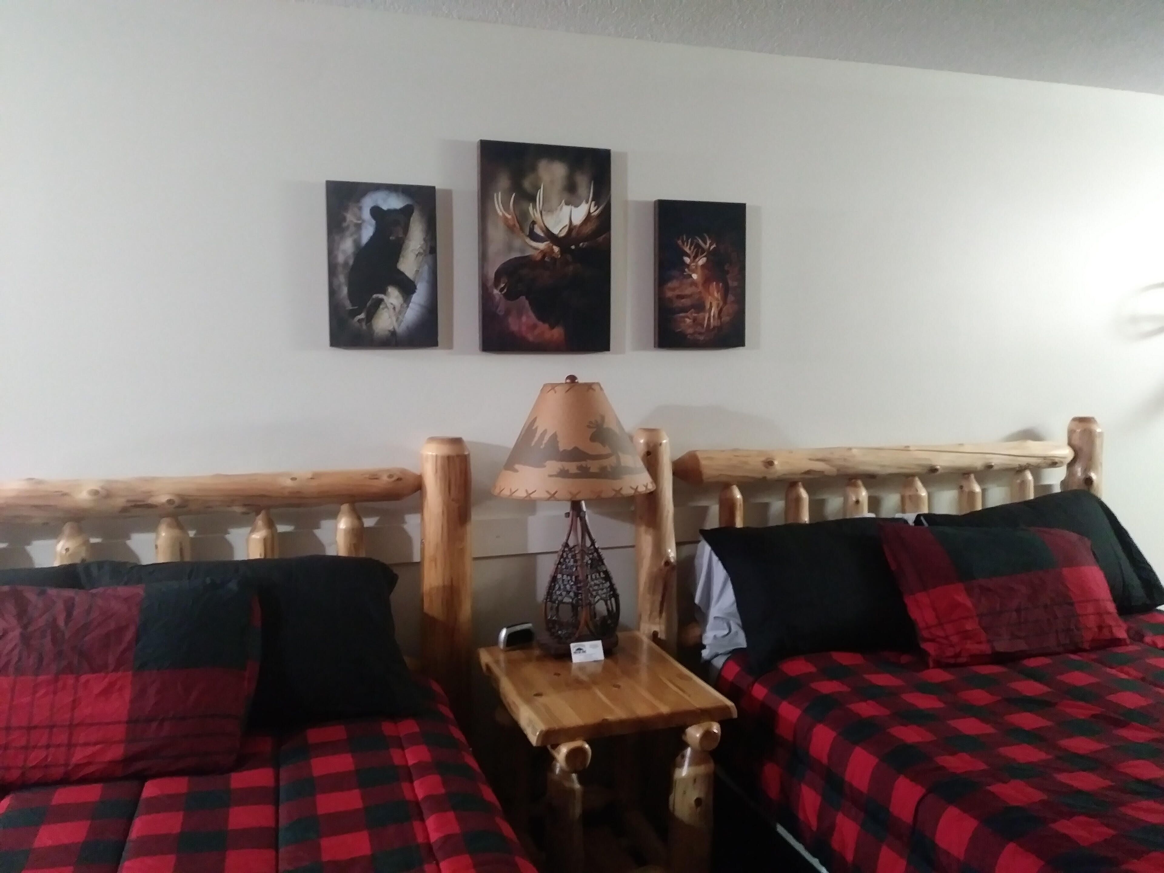 Una habitación con dos camas, un cabecero de madera, una mesita pequeña de madera y tres cuadros de animales colgados en la pared.