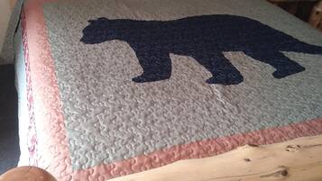 A bed with a wooden headboard and a quilt featuring a bear silhouette.