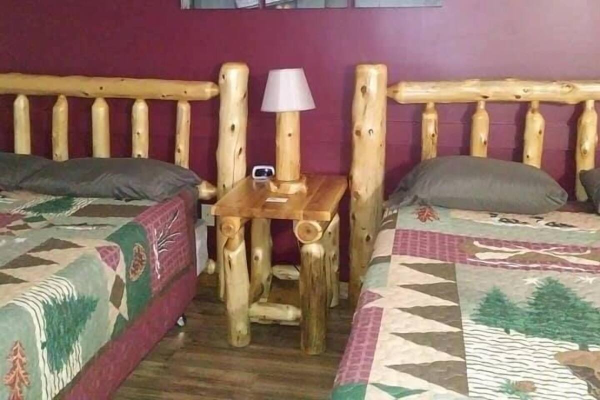 A room with two beds, a wooden headboard, a small table with a lamp, and a wall with a 'Gone Fishing' sign.