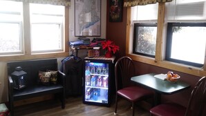 A small room with a refrigerator, a table, chairs, a bench, and a window with a map on the wall. - Briarwood Motor Inn (Lincoln)