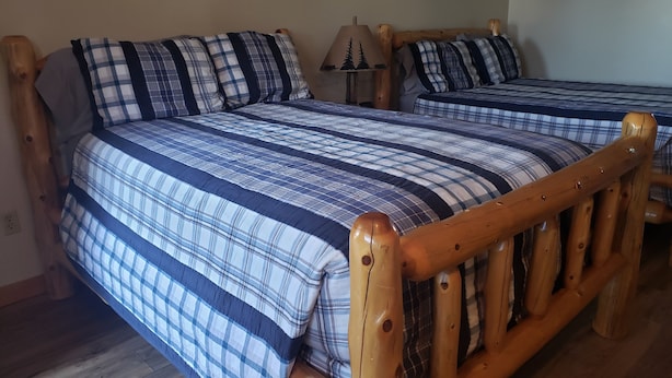 A room with two wooden beds, each with a plaid bedspread and matching pillows. - Briarwood Motor Inn (Lincoln)