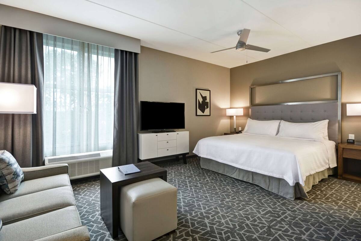A hotel room with a bed, a TV, a desk, a chair, and a ceiling fan.