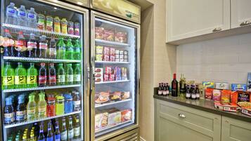 A kitchen with two refrigerators stocked with beverages and snacks, a countertop with various food items and bottles, and a cabinet with a handle.