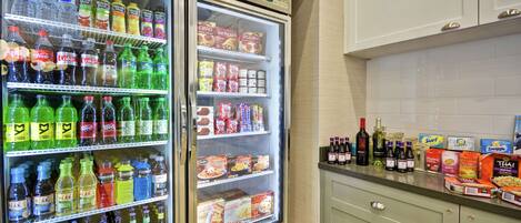 A kitchen with two refrigerators stocked with beverages and snacks, a countertop with various food items and bottles, and a cabinet with a handle.