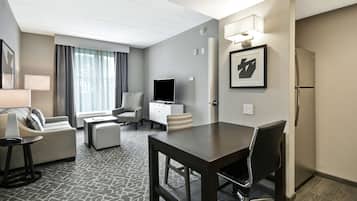 A modern hotel room with a dining area, a sofa, a TV, and a refrigerator.