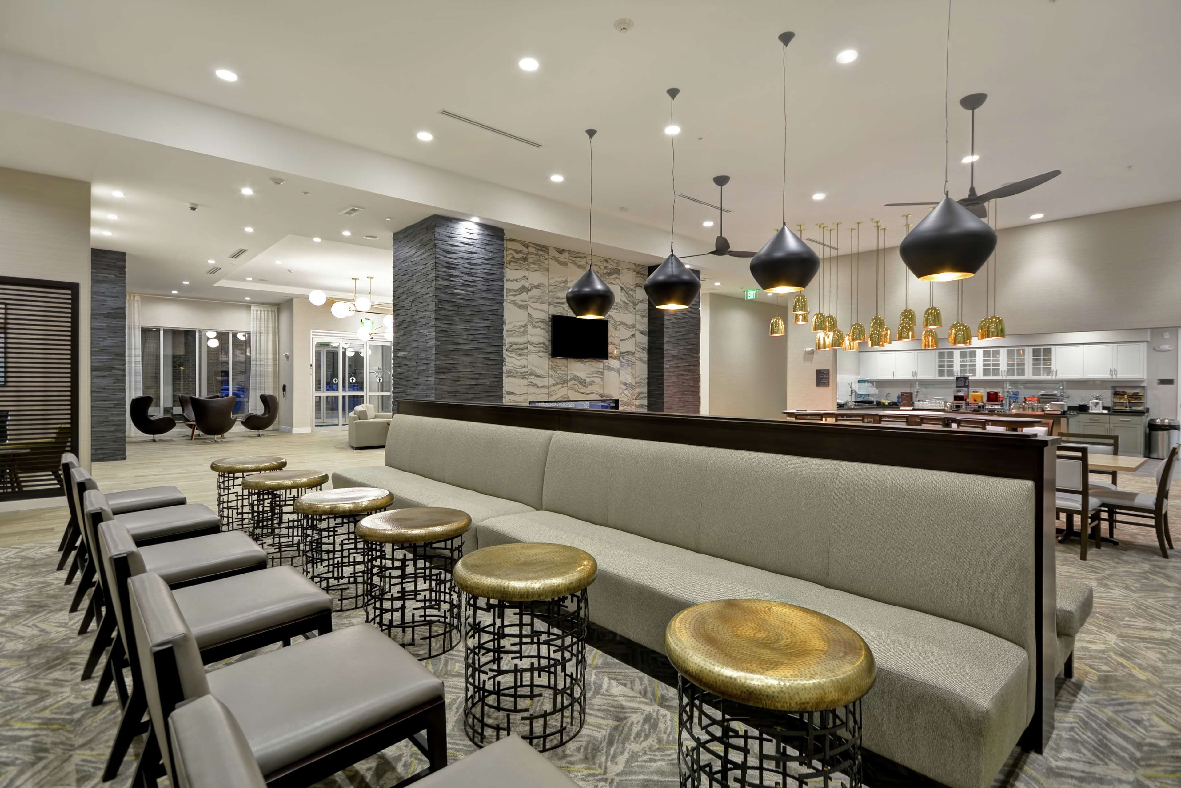 A modern hotel lobby with a seating area, a bar, and a kitchen in the background.