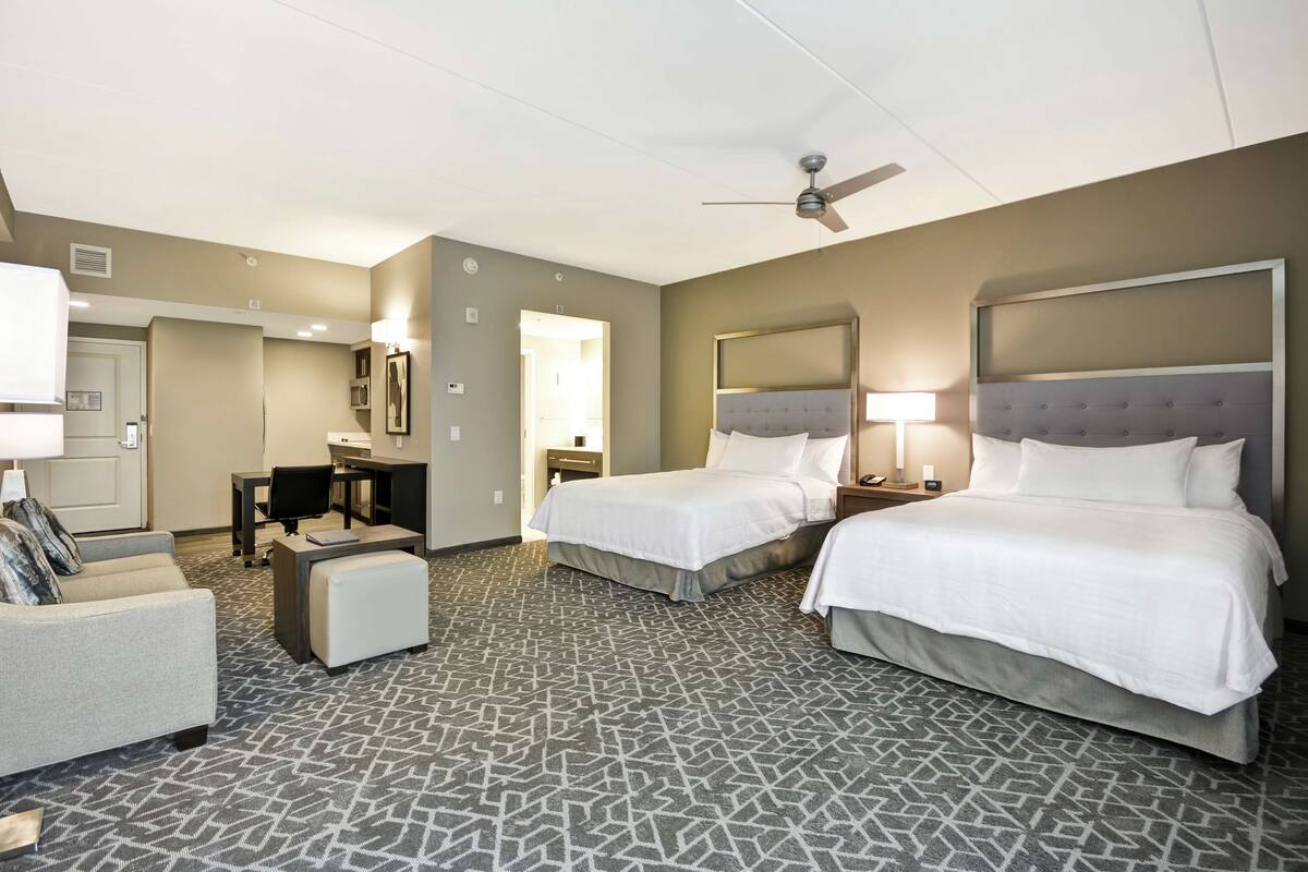 A hotel room with two beds, a desk, a chair, and a sofa.