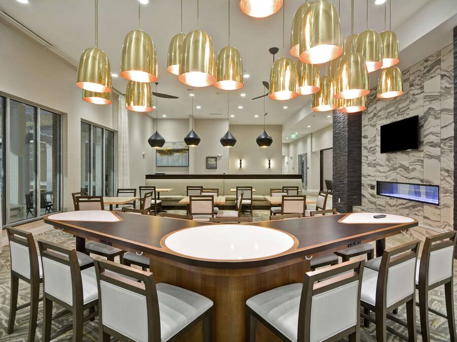A modern dining area with a large oval table surrounded by chairs, overhead pendant lighting, and a television mounted on the wall.