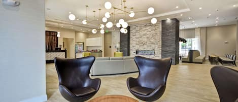 A modern lobby with leather chairs, a round wooden table, and a central light fixture.