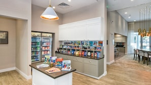 Un'area cucina moderna con isola centrale, frigorifero fornito di bevande e una varietà di snack e condimenti sugli scaffali.