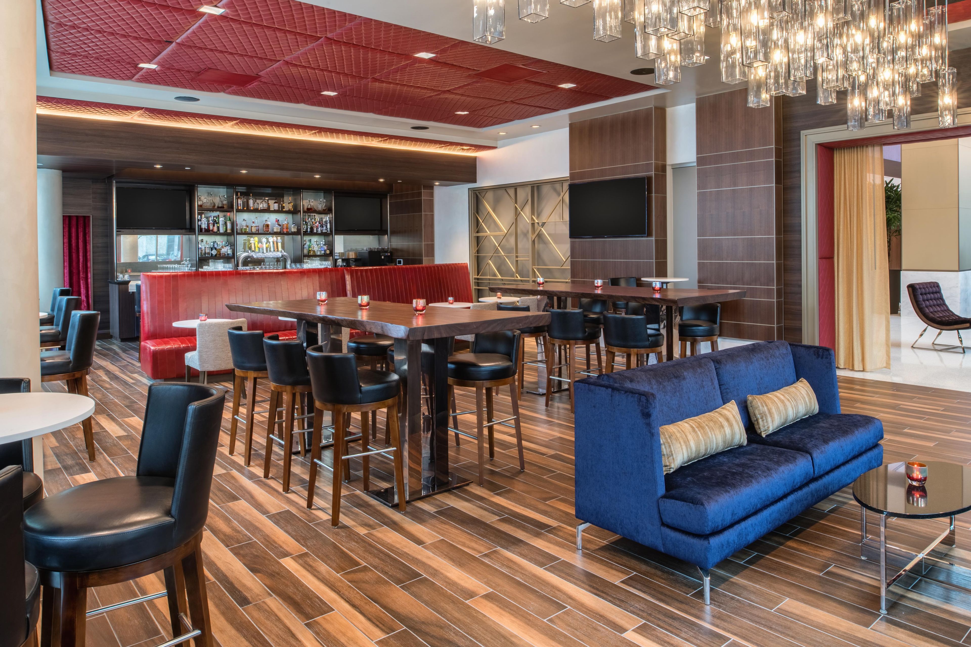 A modern bar area with a red ceiling, multiple seating options including a blue sofa and bar stools, and a variety of bar stools.